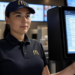 "Inside a McDonald's restaurant, a staff member interacts with the Reflexis workforce management system on a digital device, such as a tablet or wall-mounted screen. The scene includes a modern, well-lit fast food kitchen in the background, with digital menus and efficient team coordination. The interface on the screen shows employee schedules, task tracking, and shift planning. The environment should feel dynamic, tech-driven, and organized."